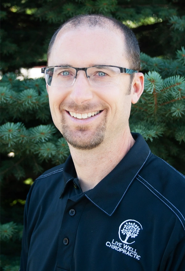 Chiropractor Brian Tolman Smiling Outdoors In Front Of Pine Tree With Attribution