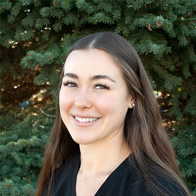 Staff Member At Live Well Chiropractic Gia Smiling In Front Of Fir Tree