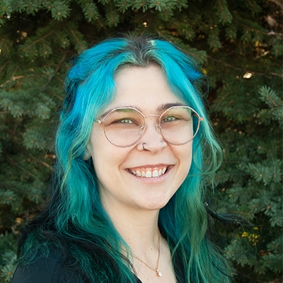 Staff Member At Live Well Chiropractic Jaycie Smiling In Front Of Fir Tree